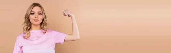 Femme souriante regardant la caméra et montrant les muscles isolés sur beige, bannière — Photo de stock