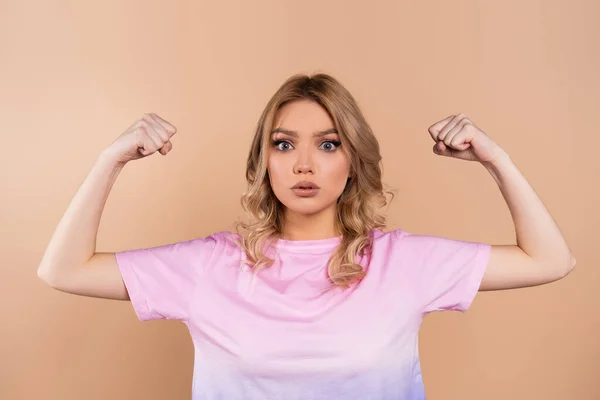 Young woman showing muscles and looking at camera isolated on beige — Photo de stock