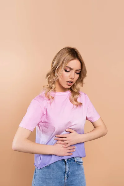 Unzufriedene Frau berührt Bauch, während sie an Bauchschmerzen leidet, isoliert auf beige — Stockfoto