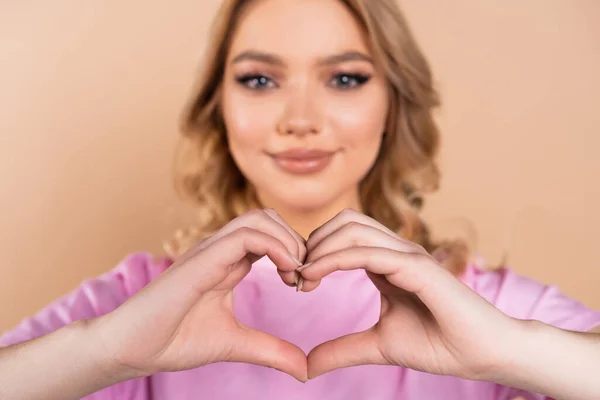 Lächelnde Frau zeigt Herzzeichen mit Händen auf verschwommenem Hintergrund isoliert auf beige — Stockfoto