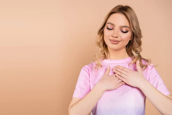 Pleased and grateful woman with wavy hair touching chest isolated on beige — Stock Photo