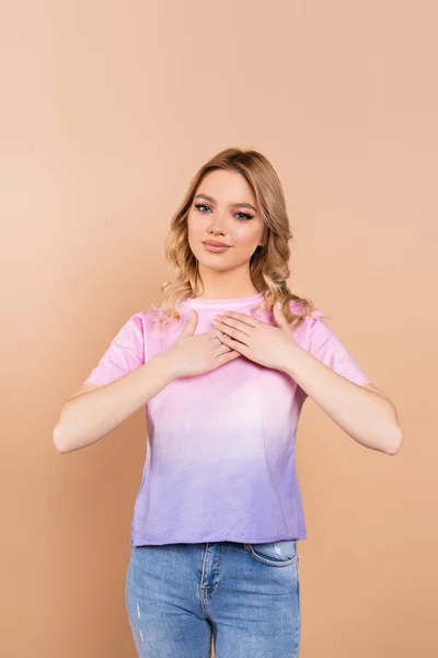 Grateful woman with wavy hair holding hands on chest isolated on beige — Stockfoto