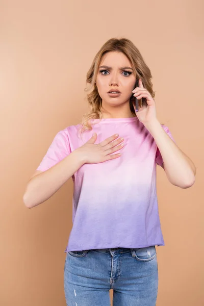 Besorgte Frau telefoniert mit Handy und berührt Brust isoliert auf Beige — Stockfoto