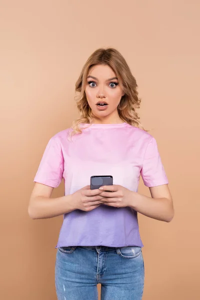 Mulher surpreso com telefone celular olhando para a câmera isolada no bege — Fotografia de Stock