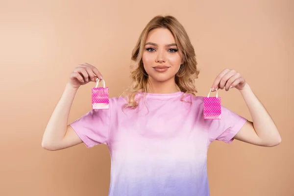 Glückliche Frau mit welligem Haar, die kleine Einkaufstüten in Beige hält — Stockfoto