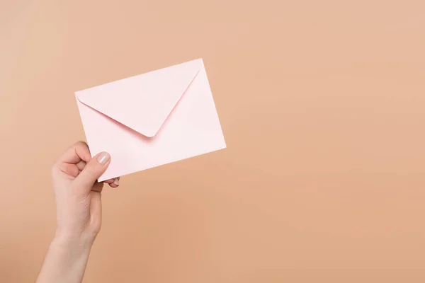 Частковий вид жіночої руки з поштовим конвертом ізольовано на бежевому — стокове фото