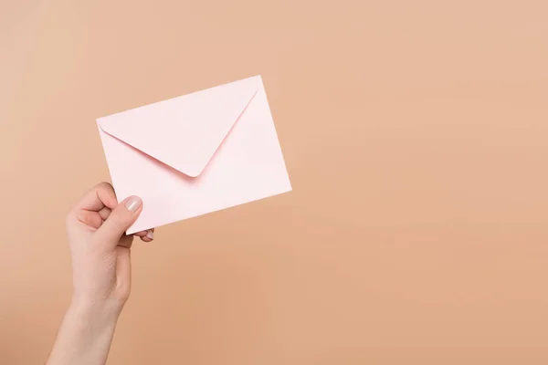 Visão parcial da mão feminina com envelope postal isolado em bege — Fotografia de Stock