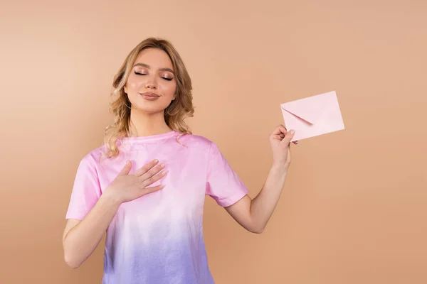 Pleased woman with closed eyes holding postal envelope isolated on beige — Foto stock