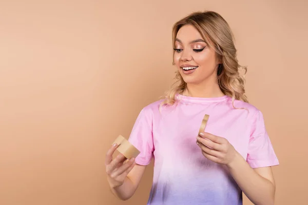 Erstaunte Frau öffnet herzförmige Geschenkschachtel isoliert auf beige — Stockfoto