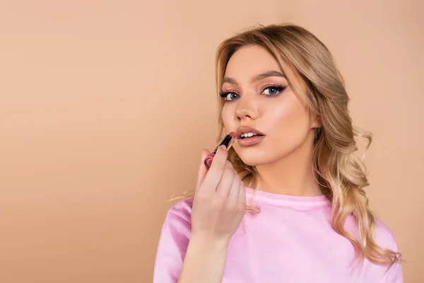 Young and pretty woman applying lipstick isolated on beige — Stockfoto