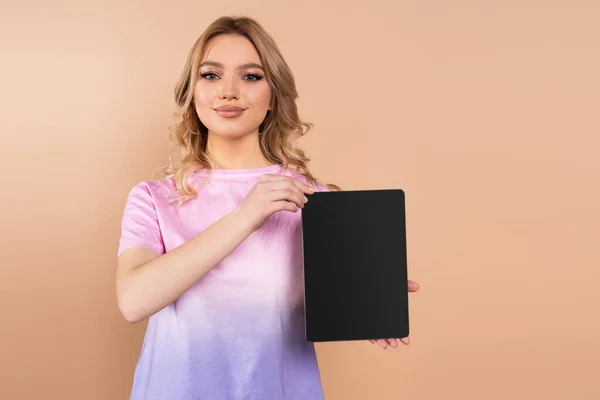 Smiling woman showing digital tablet with blank screen isolated on beige — Stockfoto