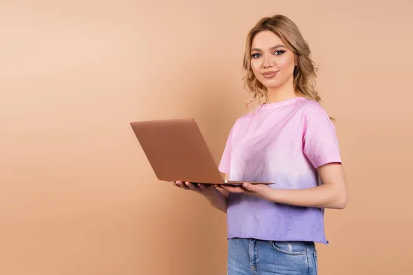 Pleased woman with laptop looking at camera isolated on beige — Foto stock