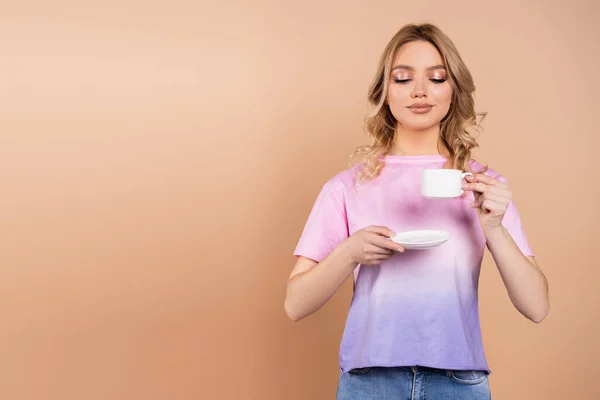 Mulher satisfeito segurando pires e xícara de café isolado no bege — Fotografia de Stock