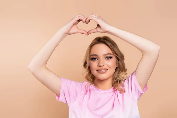 Happy woman in t-shirt showing heart sign above head isolated on beige — Stock Photo