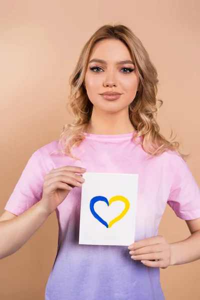 Patriotic woman showing card with blue and yellow heart isolated on beige — Stock Photo