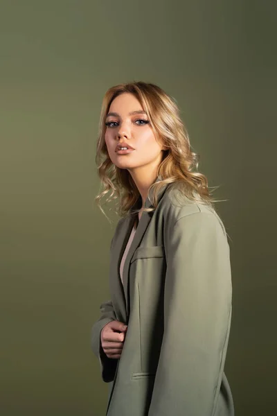 Pretty woman with wavy hair posing in oversize blazer isolated on green — Stock Photo