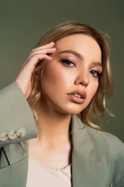 Portrait of young woman fixing hair and looking at camera isolated on green — Stock Photo