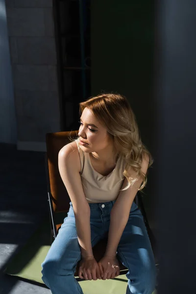 Pretty woman with wavy hair sitting on chair and looking away on blurred foreground — Stock Photo
