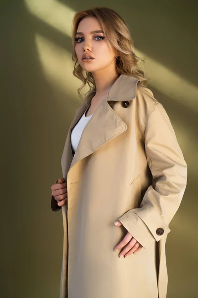 Femme élégante en trench coat regardant la caméra sur fond beige — Photo de stock