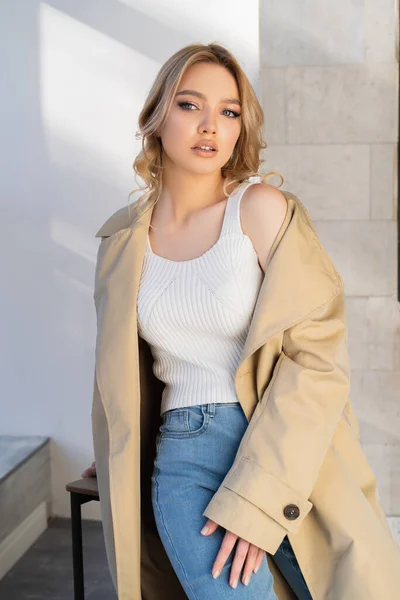 Charming woman with wavy hair looking away while posing in beige trench coat — Fotografia de Stock