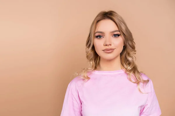 Mujer joven y bonita con el pelo ondulado sonriendo a la cámara aislada en beige - foto de stock