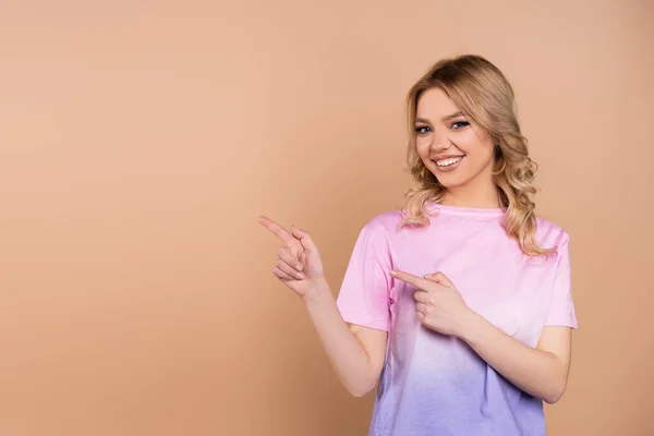 Cheerful woman pointing aside with fingers and looking at camera isolated on beige - foto de stock