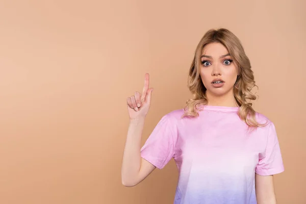 Mulher surpreso em t-shirt apontando para cima com o dedo isolado no bege — Fotografia de Stock