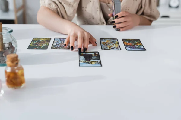 KYIV, UCRANIA - 23 DE FEBRERO DE 2022: Vista recortada de adivino usando cartas del tarot cerca de suministros de brujería en casa - foto de stock