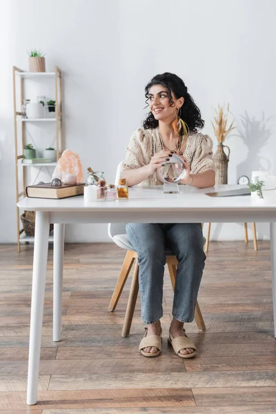 Positive Zigeuner Medium berühren Kugel in der Nähe von Buch und magischen Kristallen auf dem Tisch — Stockfoto