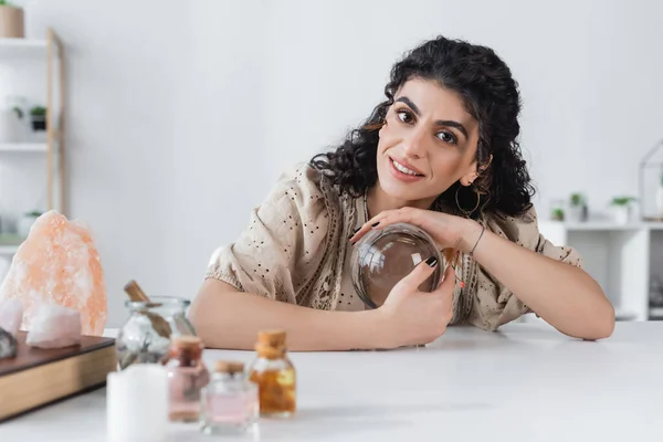 Smiling gypsy soothsayer touching orb and looking at camera at home — Stock Photo