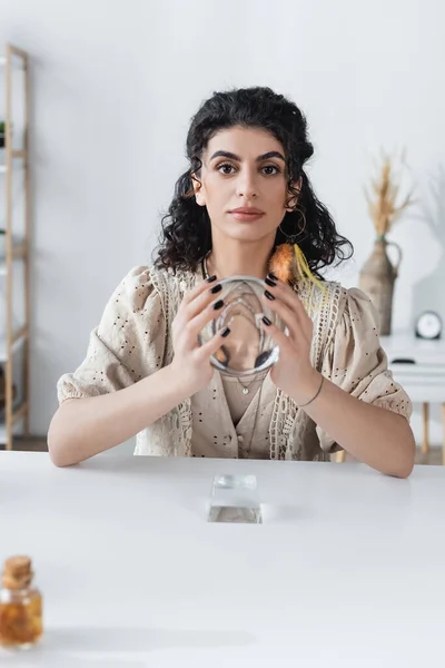 Gypsy fortune teller holding orb and looking at camera at home — Stock Photo