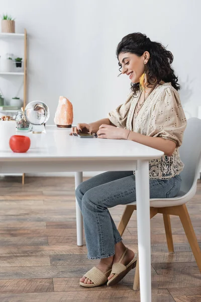 Cheerful gypsy medium looking at tarot cards near orb on table — Stock Photo