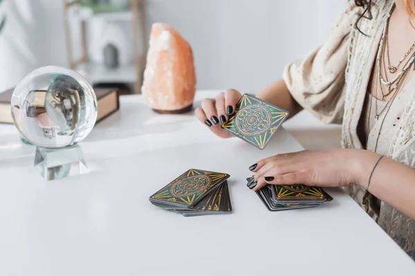 KYIV, UKRAINE - FEBRUARY 23, 2022: Cropped view of medium holding tarot cards near orb and blurred crystal on table — Stock Photo
