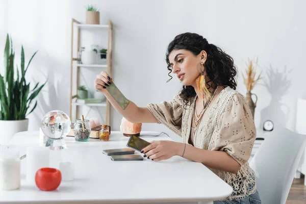 Gypsy medium holding tarot cards near candles and orb at home — Stockfoto