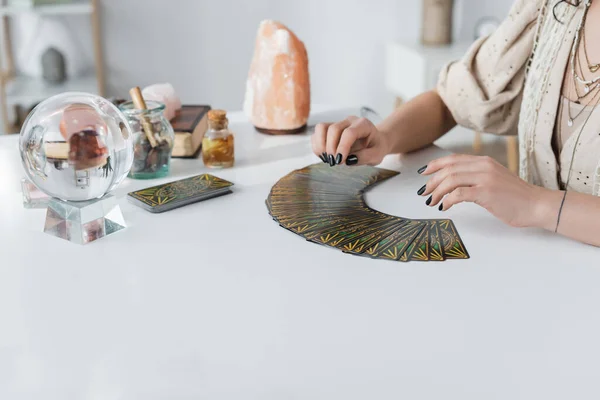 KYIV, UKRAINE - FEBRUARY 23, 2022: Cropped view of medium near tarot cards and witchcraft supplies on table — Photo de stock