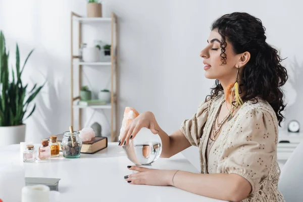 Side view of gypsy soothsayer holding magic orb near jars on table — Fotografia de Stock