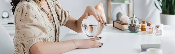 Cropped view of fortune teller touching orb near cards and jars on table, banner - foto de stock