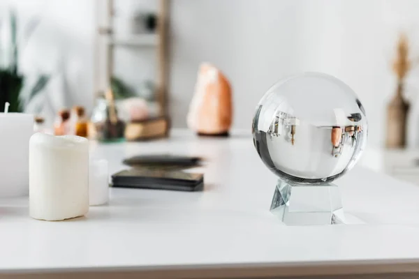 Glass orb near candles and blurred tarot cards on table — стоковое фото