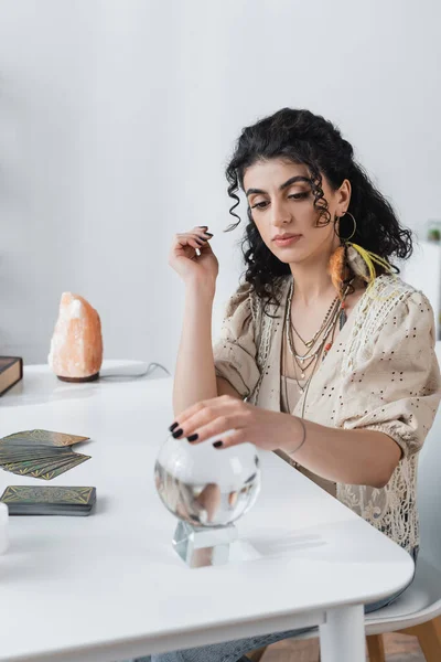 KYIV, UKRAINE - FEBRUARY 23, 2022: Gypsy fortune teller touching orb near tarot cards on table - foto de stock