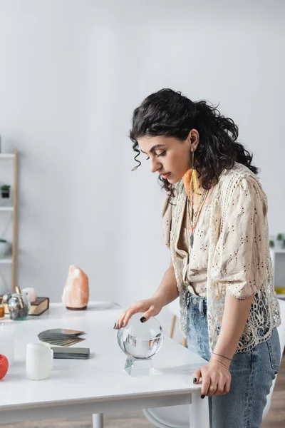 Young gypsy soothsayer touching orb near candles and cards at home — Foto stock