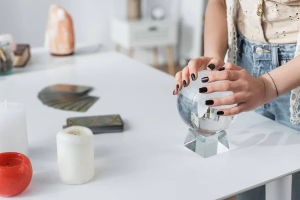 Cropped view of medium touching orb near candles on table — стоковое фото