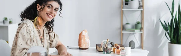 Positive gypsy fortune teller looking at camera near witchcraft supplies on table, banner — Fotografia de Stock