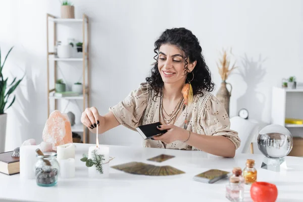 Smiling gypsy medium burning candle near witchcraft supplies on table — стоковое фото