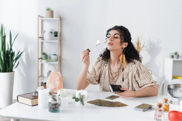 Gypsy medium blowing on match near candles and tarot cards at home - foto de stock