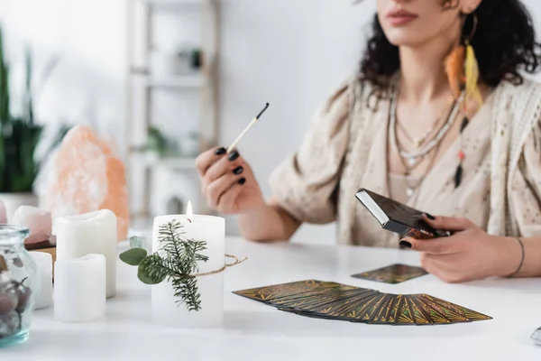 KYIV, UKRAINE - FEBRUARY 23, 2022: candles and tarot cards near blurred medium with match at home — Foto stock