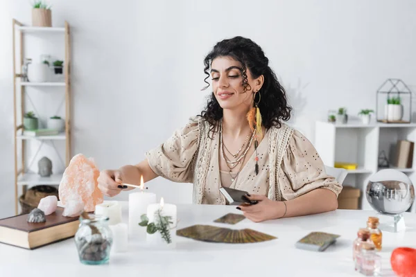 Smiling gypsy medium burning candle near tarot and jars on table — Photo de stock