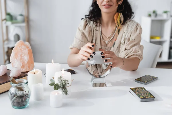 KYIV, UKRAINE - FEBRUARY 23, 2022: Cropped view of smiling fortune teller touching orb near tarot and candles — Stockfoto