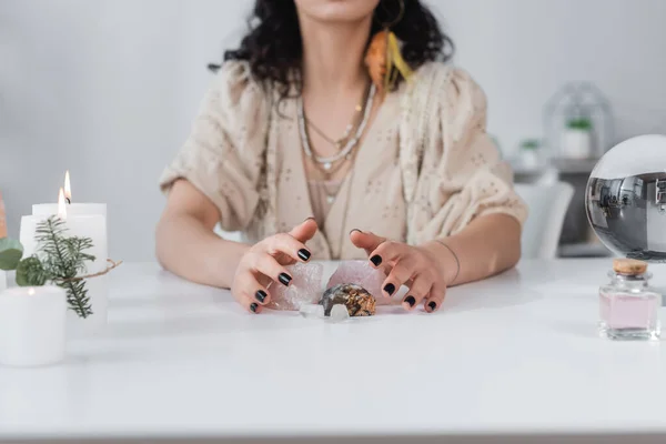 Cropped view of blurred medium sitting near magic crystals, orb and candles at home — Stock Photo