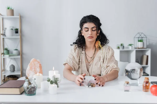 Zigeuner-Wahrsagerin berührt magische Kristalle in der Nähe von Buch, Kugel und Kerzen auf dem Tisch — Stockfoto