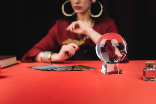 Cropped view of magic orb and tarot carts near blurred fortune teller isolated on black — Photo de stock